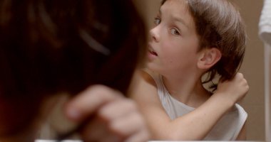 Trimming pigtails with scissors boy long hair, looks in the mirror, hand movement in bokeh. Joy on the face.