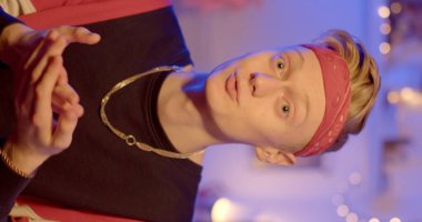 Preparing the camera and model for shooting vertical video. A guy with a bandana on his head and a chain around his neck says information. Evening room.