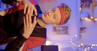 Talented guy gesticulates in conversation. He looks into the camera, tells the topic. Bandana on the head, an element of clothing. Blue light background vertical video 