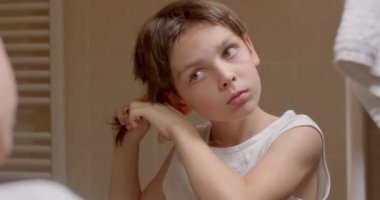Uzun saçlı makasçı çocukla örgü örmek, aynaya bakmak, Bokeh 'te el hareketi. Yüzünde neşe var. 10.11.23. CZ, Kladno, Polska