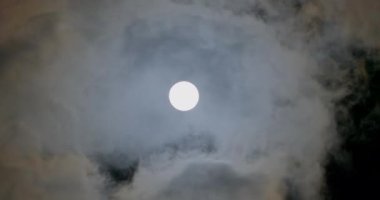 Bright disk of the moon in the night sky. Rapid movement of storm wind clouds. Dark clouds covering the light of the moon. Natural satellite of the earth night.