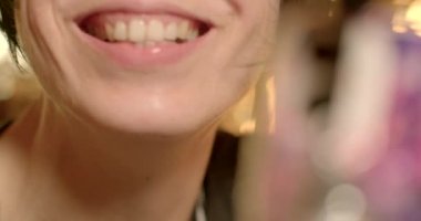 Woman shows tongue piercing into camera phone, smartphone bokeh. Two earrings, she moves, covers her mouth, smiles. Metal earrings.