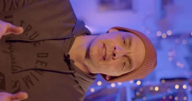 Arms folded across chest as he speaks the video to the subscribers. Consistent conversation of a muddy in a vertical frame. Blue evening background. Finger rings.