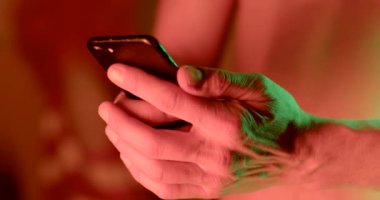Akşamları telefonu kullanan bir adamın elinin yakın çekimi. Parmaklar ekranda, mobil internet kullanımı. Kırmızı renk.