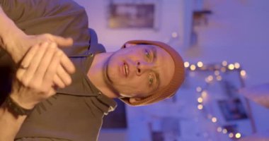 A man makes an evening video podcast. He is talking in a hat and looking at the camera. Knowledge transfer using image broadcasting. He gestures 