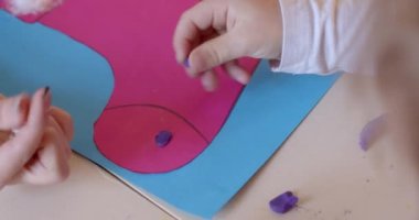 Çocuk elleri yakın çekim. Çocuklar için sanat terapisi özel oturumu. Bebek plastik modelleme kiliyle dokunmatik oyunlar oynuyor. Parmaklarda küçük nesneler. Bebek yaratıcılığını geliştirir. Pembe ve mavi kağıt..