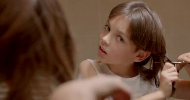 Evde aynada makasla saçlarını kesiyor. Çocuk bir tutam saç kesiyor, kendine uzun bir saç stili yapıyor. Makasın tehlikeli hareketi.