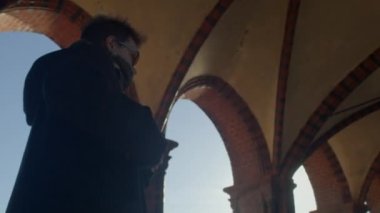 Karanlık bir cadde boyunca bir erkek yayanın hareketi. Güneş ışığı sütunların arasından parlıyor. Siyah kıyafetler. Gözlerde gözlük, rüzgar saçı. DE, Berlin, Mitte, 16.1.23. 