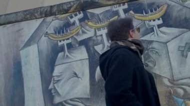 Evli bir adamın arkası, boğazdaki duvardaki resme bakar. Doğu Berlin 'in tarihi çizimi. Berlin Duvarı. DE, Berlin, Mitte, 16.1.23. 