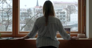 Pencerenin yanındaki kızın arkası Bokeh şehrine bakıyor. Bir psikolog olarak işten sonra dinlenmek. Eller pencere pervazında..