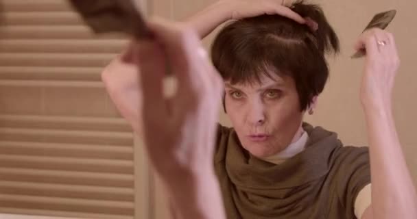 愤怒的脸女人年纪大了 她的头发在头上挠痒痒 她在家里用梳子梳起了她的头发 镜中的倒影 — 图库视频影像