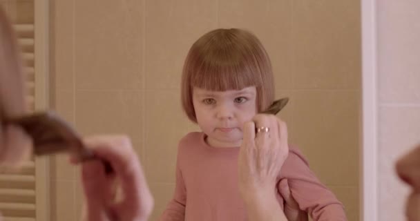 奶奶的手梳理着一个小女孩的头发 倒映在镜子里 用梳子做发型 妇女在Bokeh的年龄 — 图库视频影像