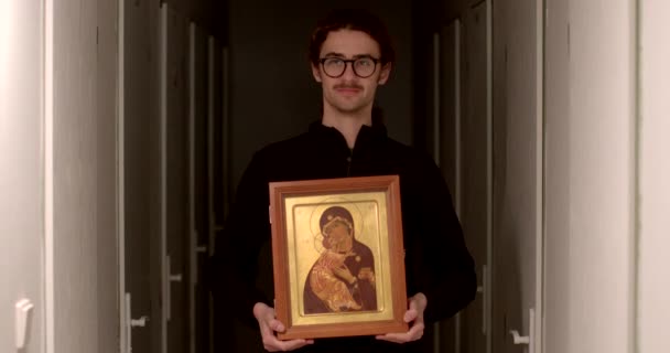 珍しいアイコンを見つけた若い男は 彼の発見を示す 宗教的な献身とテレビのポーズに使用される神聖なイメージです 聖書や聖人の生涯の物語の場面 — ストック動画