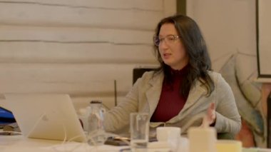 Uzun saçlı, gözlüklü bir kadın masada dizüstü bilgisayar kullanıyor. Bilgiyi sözlü olarak konuşuyor, kafasını oynatıyor. 25.02.2023 Rackunai. Litvanya