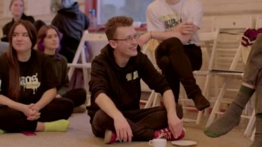 Öğrenim görürken bir grup öğrenci yerde oturuyor. Gözlüklü bir adam tabaktan abur cubur yer. Rahat seminer atmosferi. 25.02.2023 Rackunai. Litvanya