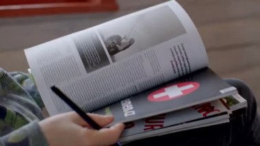 Okuyucular bir gazete yasallaştırma dergisinin sayfalarına bakıyorlar. Resimlere hızlı bir bakış, sayfa araması. Bokeh dilinde kalem. Yazılı madde kullanımı. 25.02.2023 Rackunai. Litvanya