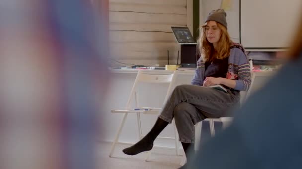 女讲师坐在椅子上讲话 她在提供信息时做手势 Bokeh效应使听众旋转 帽子在头上 2023 Rackunai 立陶宛 — 图库视频影像