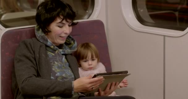 受到启发的妈妈在地铁里和女儿一起用平板电脑 她手里拿着乐器 专注在屏幕上 火车运动 公共交通工具的空闲时间 — 图库视频影像