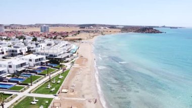Güneşli bir tatil köyünün kumsalında. Yüzmek için mavi okyanus suyu. Ebb ve akıntı kıyıları yıkar. Drone kamera hareketi. Gökyüzü ufku.