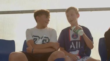 İki genç futbolcu tribünde poz veriyor. El su içmek için bir şişe kullanarak bir jest gösteriyor. Su dengesi yenileniyor. CZ, Sunucu 15.6.24