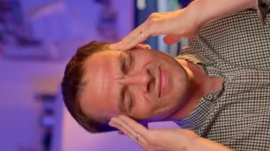 Modern ofis ortamında stres ve baş ağrısı çeken, başını rahatsızlık içinde tutan bir adam..