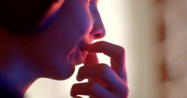 Dudağına eliyle dokunur, derin düşüncelere dalmış bir insanı arkaplanda canlı bir ışıkla yakalar, derin düşüncelere dalmış bir atmosferi oluşturur.