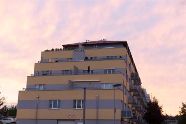 Büyük ve etkileyici bir bina ihtişamlı bir şekilde ayakta duruyor. Arkaplanda gökyüzünü aydınlatan canlı bir günbatımı var. Güzel renkler sergiliyor.