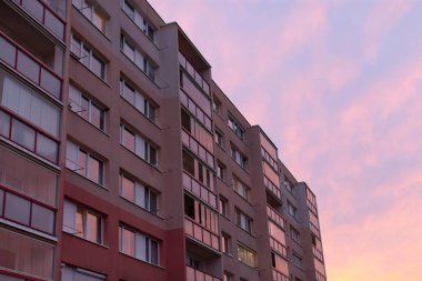 Büyük ve etkileyici bir apartman, akşam gökyüzünde gün batımının canlı zeminine karşı dimdik ayakta duruyor.