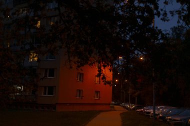 Sayısız pencereyle süslenmiş canlı kırmızı bir bina gece çok güzel aydınlatılır ve akşam ortamına sıcak bir ışık saçar.