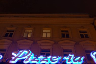 Parlak neon ışıklı bir tabela içeren seçkin bir bina var. Geceleri herkesin görebileceği bir pizzacı kelimesini açıkça gösteriyor.