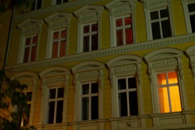 Sayısız büyük pencereyle süslenmiş canlı sarı bir bina gece çok güzel aydınlatılır ve büyüleyici bir şehir atmosferi yaratır.
