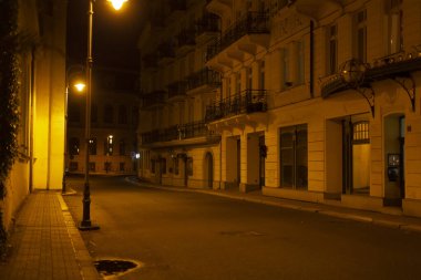 An empty street during the night hours, with tall buildings lining both sides and the stillness amplifying the isolation of the area clipart