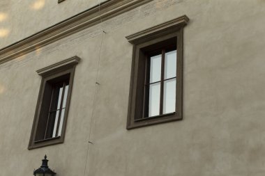 Kentsel bir ortamda, iki zarif çerçeveli kahverengi ahşap pencere, mükemmel bir şekilde yerleştirilmiş, desenli bej bir duvarda, etrafındaki güneş ışığını güzel yansıtıyor, genel havayı güzelleştiriyor.