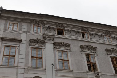 Tarihi bir binanın ön cephesi, dikkat çeken çok sayıda güzel tasarlanmış pencerenin yer aldığı, karmaşık ve süslü mimari detayların çarpıcı bir gösterisini sunuyor.