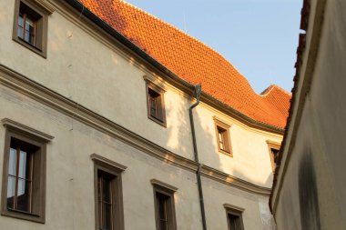 Tarihi bir binanın güzel kıvrımlı cephesinde zarif pencereler ve çarpıcı kırmızı bir çatı bulunur. Mavi gökyüzü ile çelişir ve eşsiz mimari detaylarını gözler önüne serer.