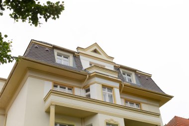 Geniş, büyük, siyah çatılı beyaz bir ev ve çevreyi harika bir şekilde gören güzel bir balkon.