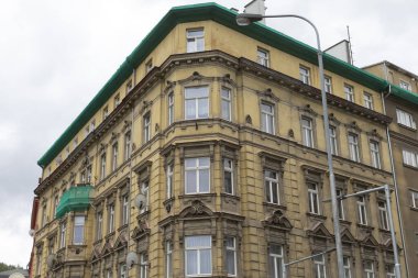 Belirgin yeşil çatısı ile karakterize edilmiş büyük, etkileyici bir bina var ve önünde bölgeyi aydınlatan uzun bir sokak lambası duruyor.