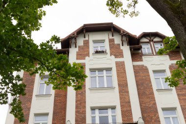 Büyük ve heybetli bir tuğla bina belirgin duruyor, önünde güzel yeşil bir ağaç duruyor, cazibe ve karakter ekliyor.