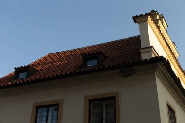 Evlerin çatısı belirgin kiremit elementler ve açık mavi gökyüzüne karşı açılan belirgin bir baca içerir.