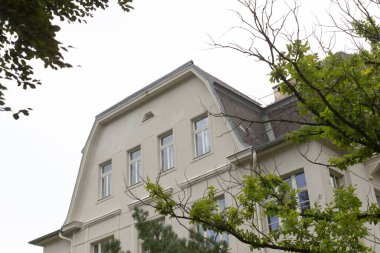 Tarihi binanın arka planında yemyeşil ağaçlarla çevrili pencereli güzel bir cephesi var.