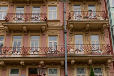 Balkon ve pencerelerin dokulu arka planda yer aldığı tarihi bir binanın cephesi.