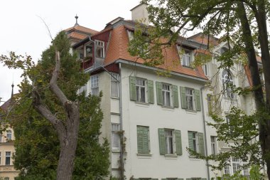 Güzel yeşil panjurları ve çarpıcı kırmızı çatısı olan büyüleyici beyaz bir bina var. Bu da bölgede önemli bir manzara oluşturuyor.