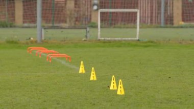 Bir futbol antrenmanı kurulumu arka planda bir amaç olan çimen sahasında düzgünce düzenlenmiş kozalakları içerir.