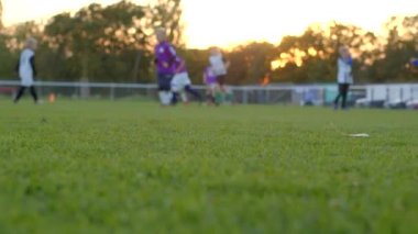 Bokeh etkisi, atletlerin hareketi. Genç futbolcular gün batımında canlı bir çimenlikte aktif olarak birbirleriyle yarışıyorlar.