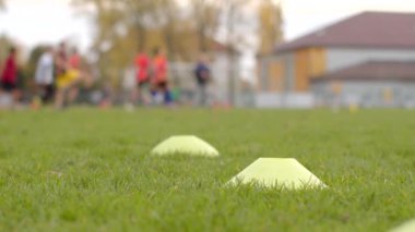 Bokeh 'te arka planda aktif olarak yer alan birden fazla koni ve oyuncuyla donatılmış bir futbol antrenman sahası. Bir grup sporcu antrenman yapıyor.