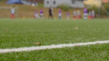 Sentetik çim tarlasında bir genç futbol maçı devam ediyor. Gelişmiş bir atmosfer yaratıyor. Çimlere işaretler yapıştırıyor.