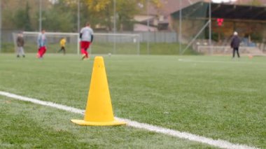 Sahada sarı koni. Gençlik futbol antrenmanı canlı sahada. İstekli oyuncular ve antrenman konileri var.