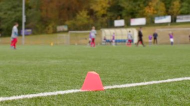 Spor sahasının bitiş noktası, arka planda oyuncuların görüldüğü bir çim sahasındaki kozalakların yer aldığı bir futbol antrenmanı düzeneği ile işaretlendi..