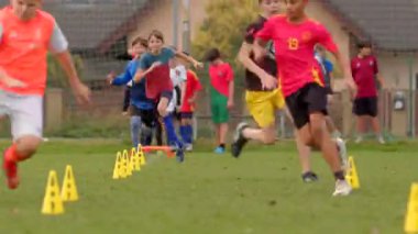 Genç futbolcular geniş bir alanda beceri tatbikatı yapıyor. CZ arka planına renkli koniler saçılmış, 10.24 ev sahibi yok.