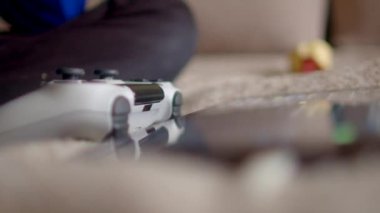 Oturma odasında, bir oyun kumandası koltukta görünür bir mobil cihaz ile oyun düzeneğini gösteriyor.